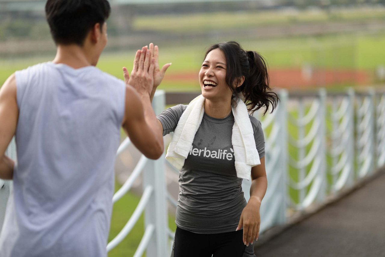 Two young people stretch to warm up before jogging and high-five each other in the park