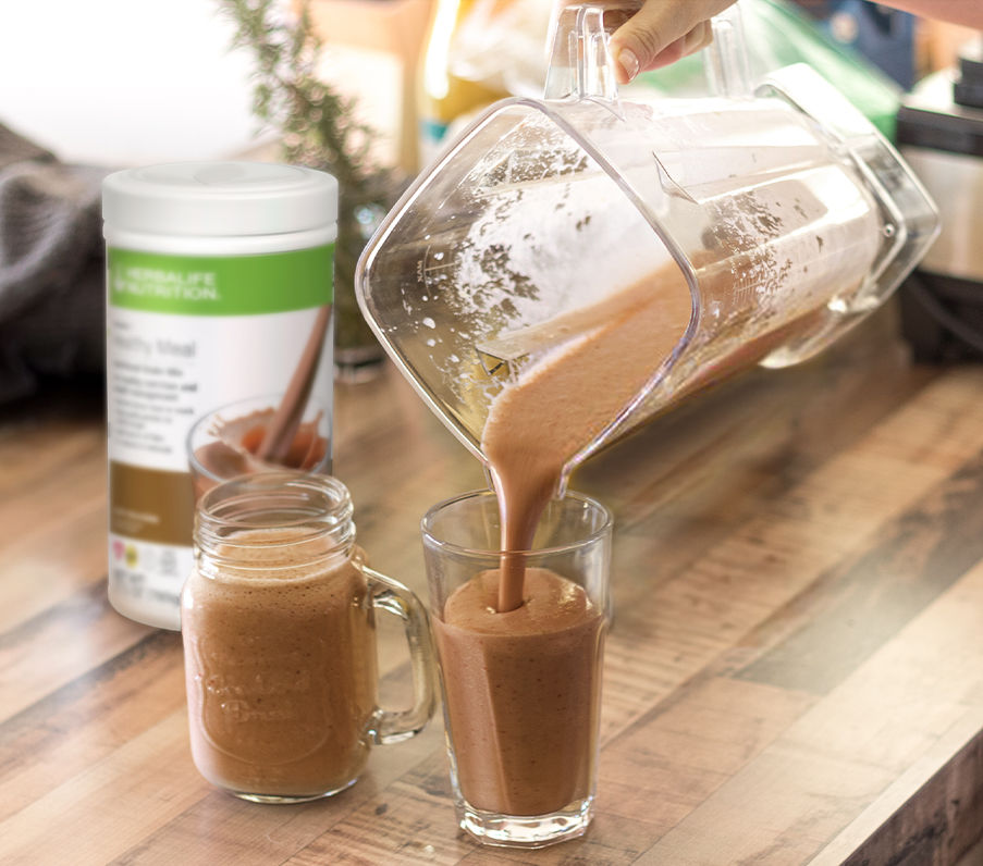 Chocolate shake being poured from blender into a glass and a jar