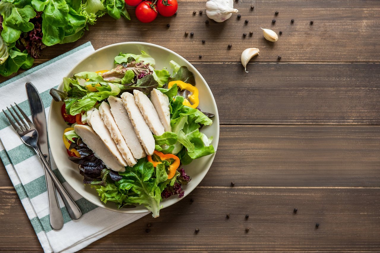 Healthy food, ready to eat mix fresh vegetable salad with skinless boiled chicken breast, top view on wood table background  with copy space